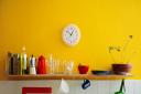 Yellow wall with utensils on a shelf and wall clocks.
