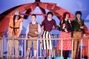 The cast of James And The Giant Peach on board a huge piece of wooden fruit at Watford Palace Theatre