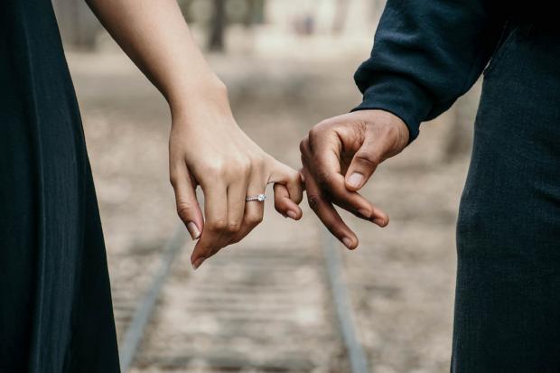 St Albans & Harpenden Review: A couple linking fingers while she wears an engagement ring. Credit: Canva